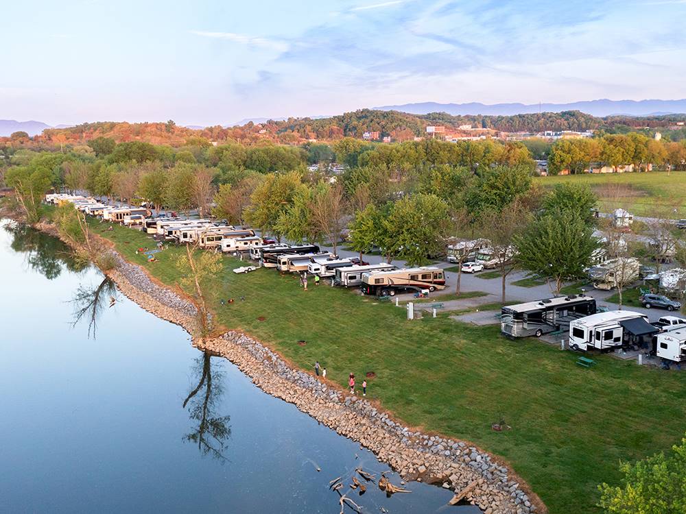 A row of RVs backed in at sites near the river at RIVERSIDE RV PARK & RESORT