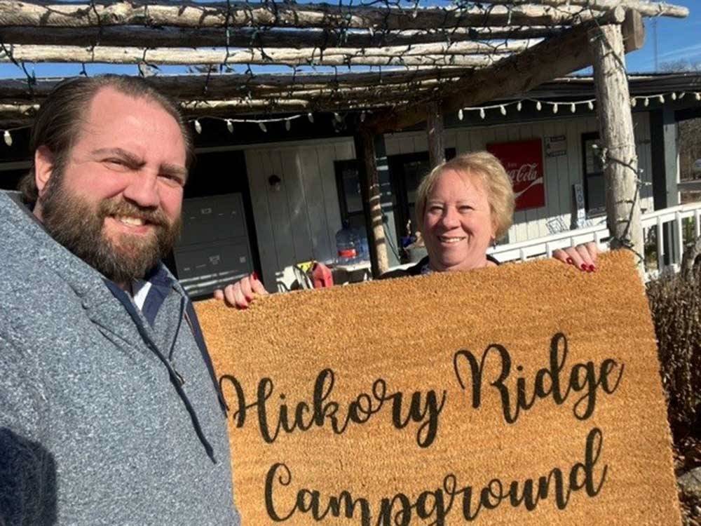 A couple holding up a mat with the campground name on it at HICKORY RIDGE CAMPGROUND