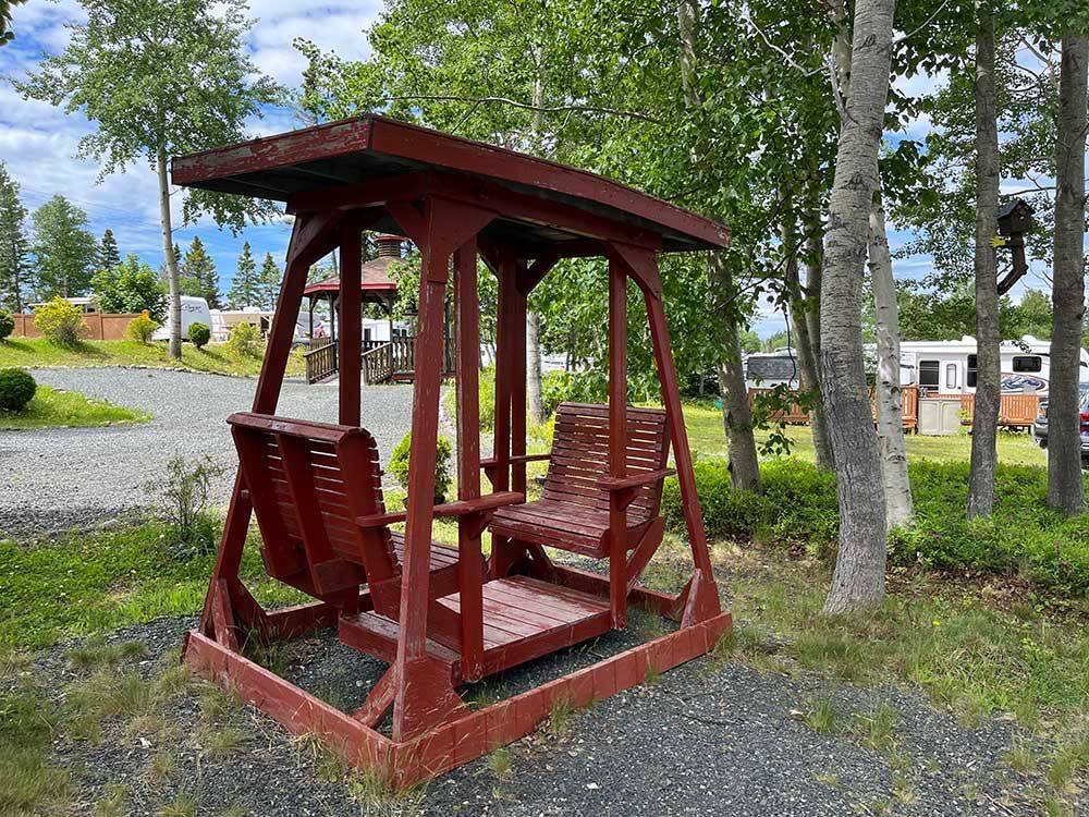 A red bench swing under trees at HAROLD W. DUFFETT SHRINERS RV PARK