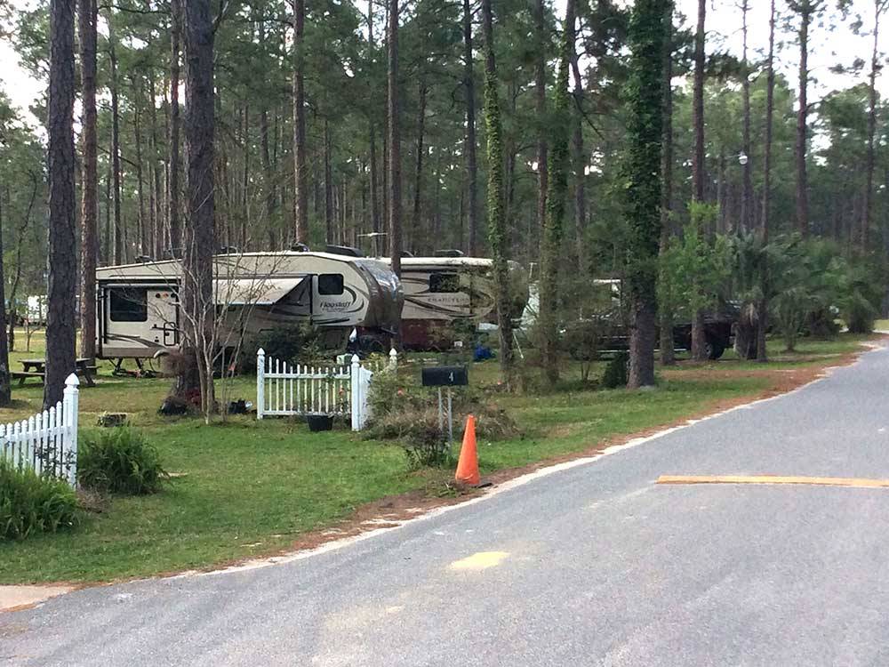 Trailers camping among tall trees and white picket fences at SUGAR MILL RV PARK