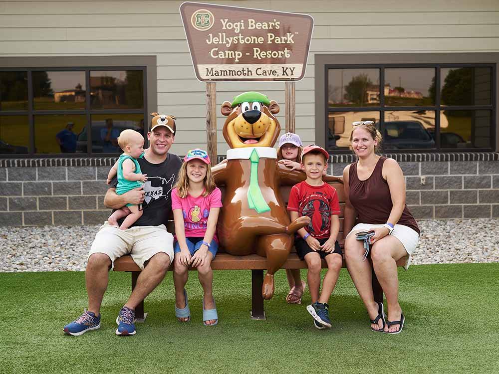 Family sitting on a bench with a Yogi Bear statue at JELLYSTONE PARK AT MAMMOTH CAVE