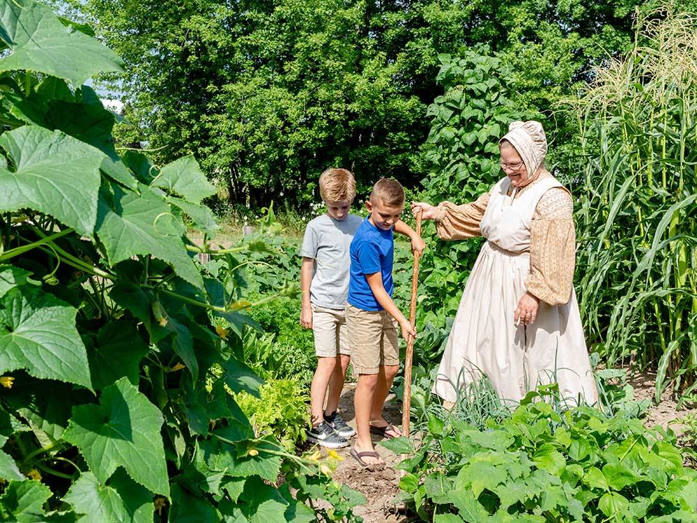A lady showing two boys how to farm at SAUDER VILLAGE CAMPGROUND