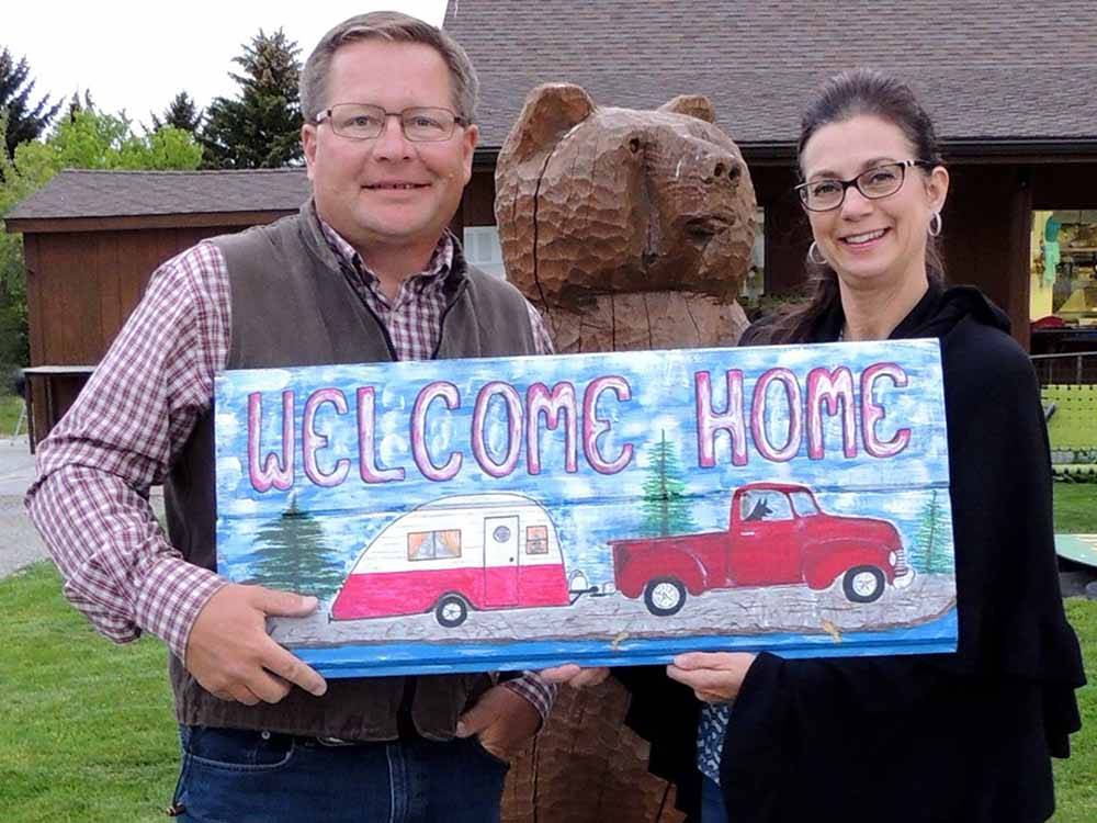 A couple holding up a Welcome Home sign at YELLOWSTONE'S EDGE RV PARK
