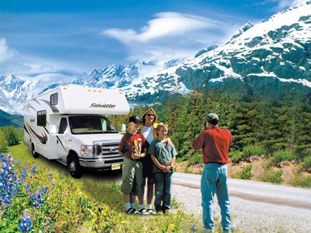 Man taking photos of family in front of RV with mountains in background at ANCHORAGE SHIP CREEK RV PARK