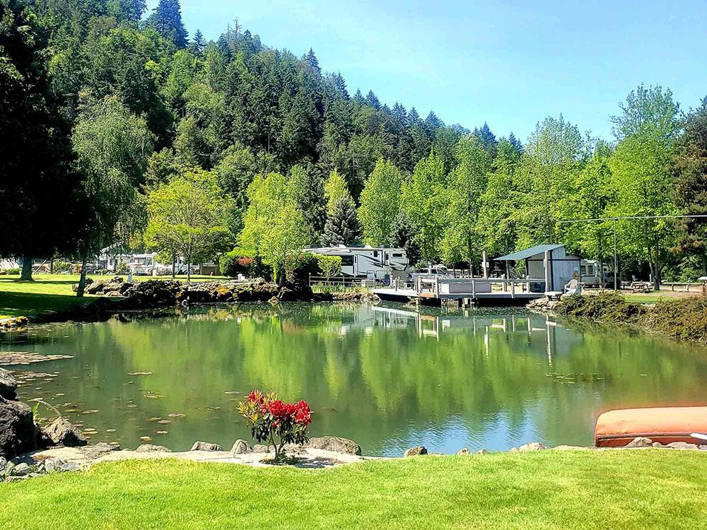 Large pond, flowers, trees, RVs, evergreen mountain in background at ON THE RIVER GOLF & RV RESORT