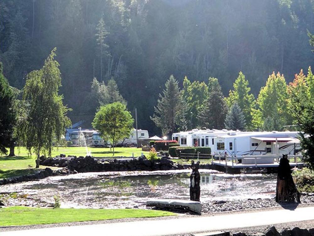 Large pond, RVs and an evergreen mountain backdrop at ON THE RIVER GOLF & RV RESORT