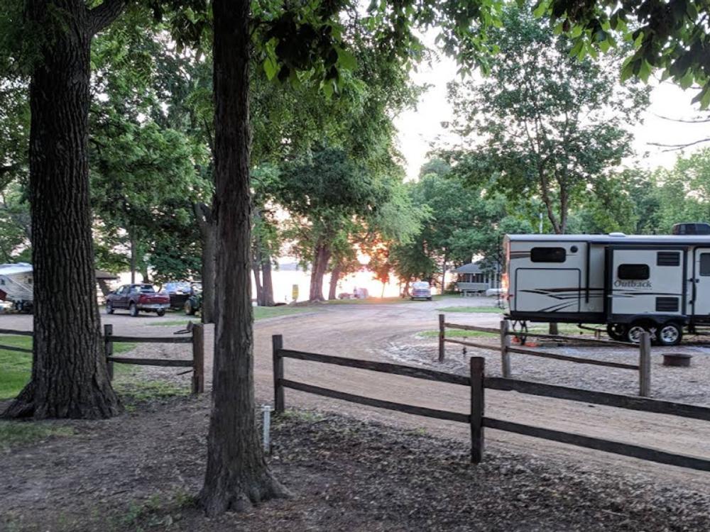 Travel trailer parked on gravel site near a lake at sunset at Lakeshore RV Park