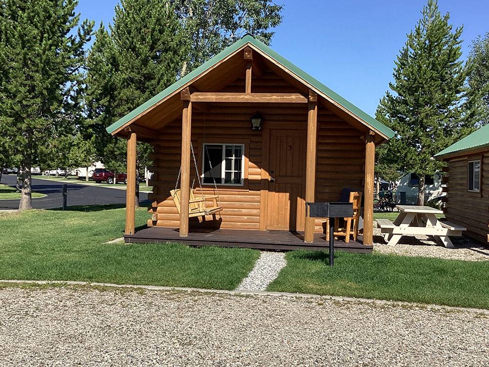 A wooden cabin with a swing on the deck at YELLOWSTONE GRIZZLY RV PARK