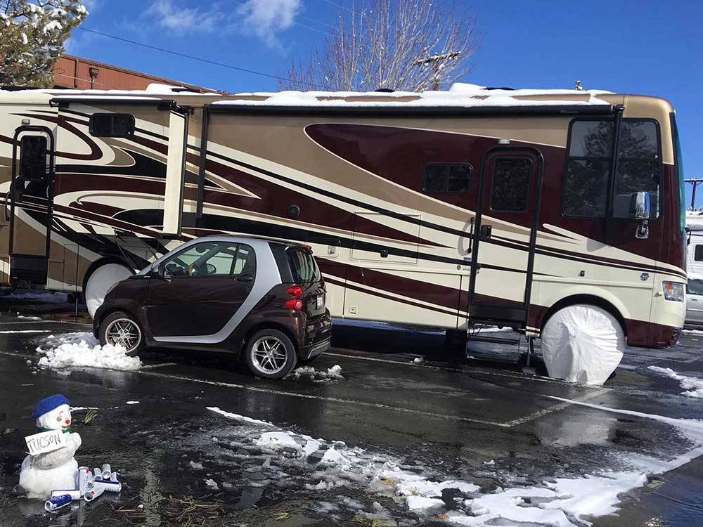 Burgundy and tan Class A motorhome parked in a snowy lot next to a snowman at SILVER SAGE RV PARK