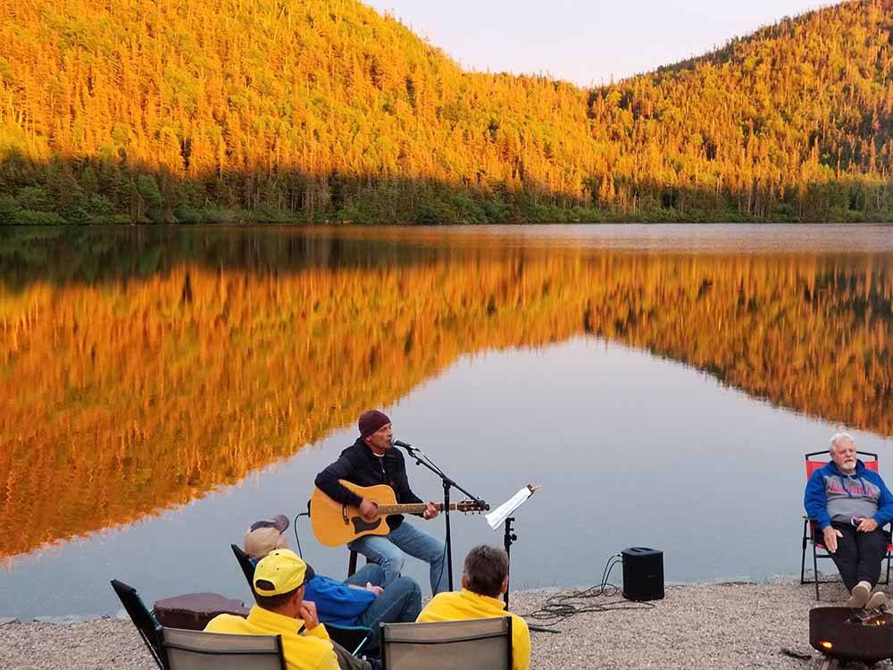 A man playing a guitar next to the water at GROS MORNE/NORRIS POINT KOA