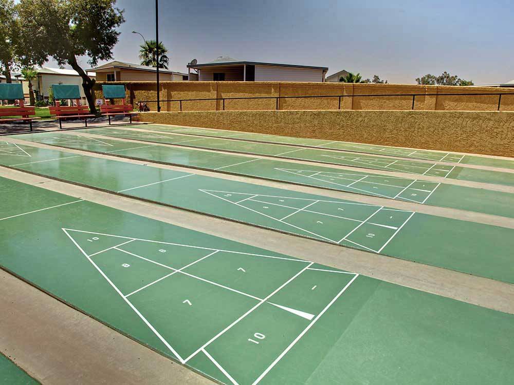 Green shuffleboard courts surrounded by a brick wall and trees at SUNRISE RV RESORT
