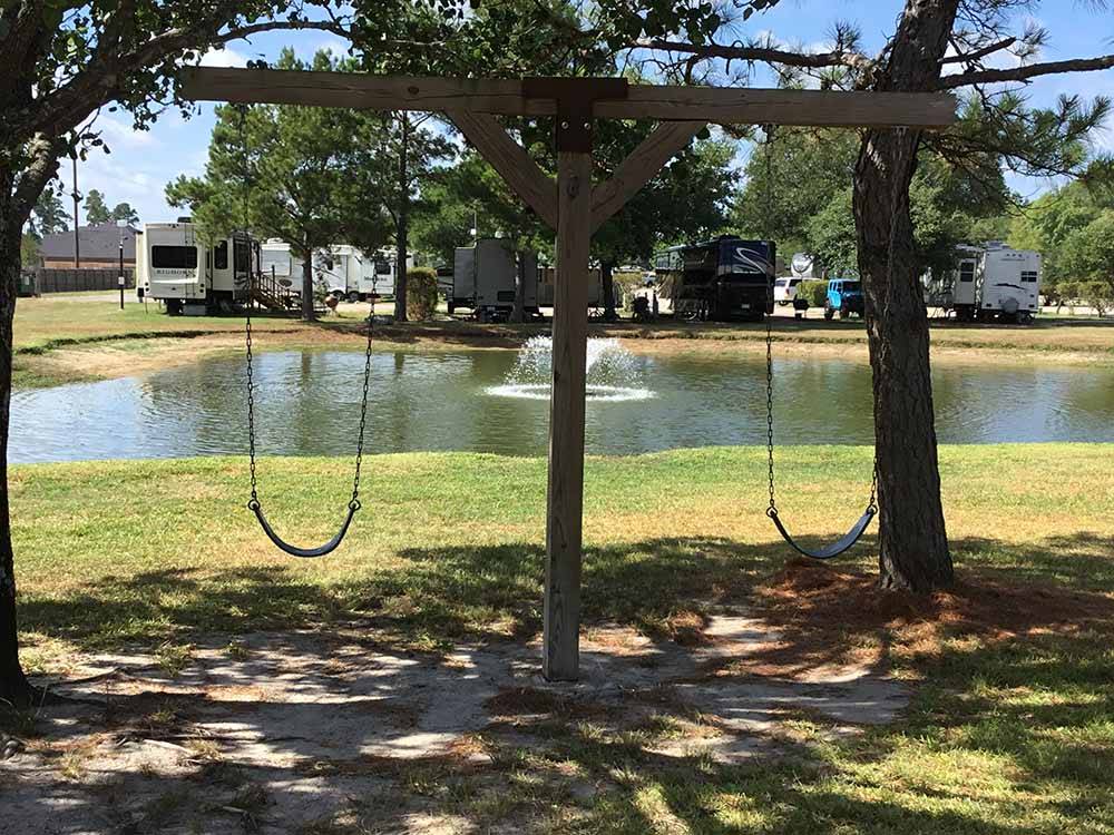 A fountain in the middle of a pond with RVs and swing set on banks at WOODLAND LAKES RV PARK