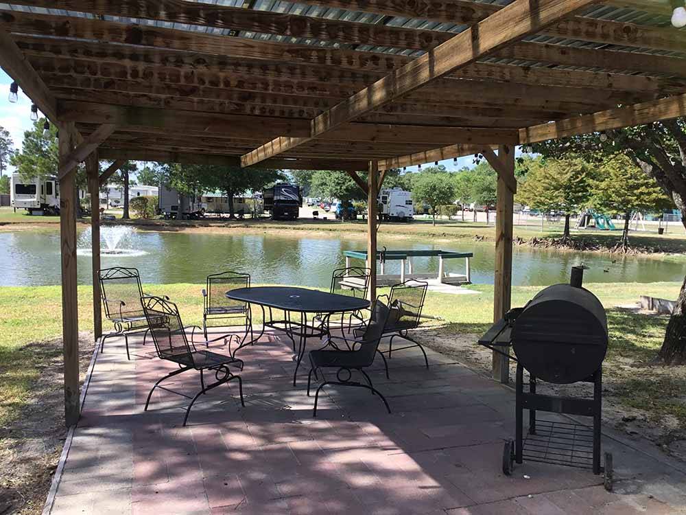 Table and chairs under canopy near pond at WOODLAND LAKES RV PARK