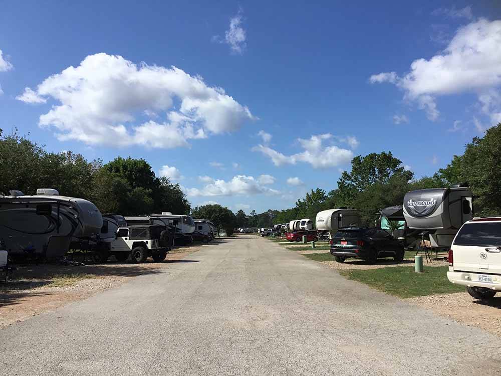 Campground road flanked by campsites under blue sky  at WOODLAND LAKES RV PARK
