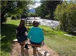A couple of people sitting on a bench looking at the river at MANOR RV PARK - thumbnail
