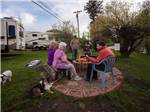 People around a fire pit with a dog at MANOR RV PARK - thumbnail