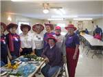 View larger image of Women with red hats standing around craft table at HO HO KAM RV PARK image #6