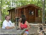 A couple sitting in front of a rustic rental cabin at INDIAN CREEK CAMP & CONFERENCE CENTER - thumbnail