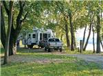 RV and truck in a treed site with lakeview at MILLPOINT RV PARK - thumbnail