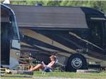 View larger image of A woman sitting outside of a motorhome reading a book at CIDER HOUSE CAMPGROUND image #3