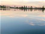 View larger image of Placid lake reflecting sky with buildings on distant bank at WAKESIDE LAKE RV PARK image #4
