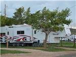 Triple-axle fifth-wheel with tree in foreground at NO NAME CITY LUXURY CABINS & RV PARK - thumbnail