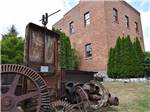 View larger image of A piece of rusty machinery in front of a brick building at NICOLSTON DAM CAMPGROUND  TRAVELLERS PARK image #1