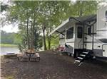 Travel trailer parked by the river with a bench at WENDY OAKS RV RESORT - thumbnail