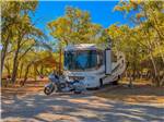 An RV and motorcycle parked in a paved site at Hidden Cove Park - thumbnail