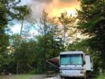 View larger image of RV backed in a site with sunset behind the tall trees at MOOSE HILLOCK CAMPING RESORT NY image #2