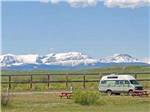 Camping van with towering snow-capped mountains on horizon at SLEEPING WOLF CAMPGROUND & RV PARK - thumbnail
