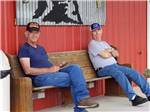 Two men sitting on a bench by the front building at RV CORRAL - thumbnail