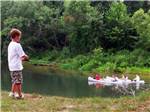 View larger image of Boy fishing as people kayak in distance at HIDDEN SPRINGS RV RESORT image #1