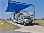 A Class C motorhome parked under a shade at JETSTREAM RV RESORT - TROPICAL TRAILS - thumbnail
