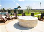 A large cement fire pit with lounge chairs at JETSTREAM RV RESORT - TROPICAL TRAILS - thumbnail