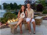 A couple and their dog sitting next to an open fire at MOTORCOACH RESORT LAKE ERIE SHORES - thumbnail
