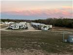 View larger image of Looking down the row of RVs with pink clouds on horizon at BANDERA CROSSING RIVERFRONT RV PARK image #6