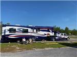 View larger image of A couple siting along side of a very large fifth wheel trailer at BIG RIG FRIENDLY RV RESORT image #1