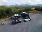 RVs and cars parked in a site over looking a forested valley - thumbnail