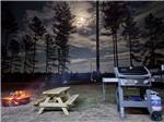 A barbecue pit and bench next to a fire pit lit at DREAM RV PARKS - thumbnail