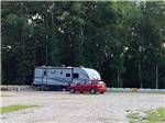 A red car and trailer parked in a site at KELLY CREEK RV PARK - thumbnail
