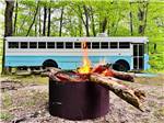 A burning fire pit with a bus in the background at DANCING FIRE GLAMPING AND RV RESORT - thumbnail