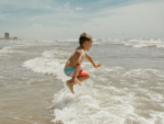 Child jumping in the waves at Corpus Christi Boardwalk RV Park - thumbnail