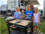 A dad and his children cooking bacon on the grill at WORLD WIDE TECHNOLOGY RECEWAY CAMPGROUND - thumbnail