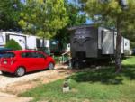 A red car parked behind a trailer in a RV site at BROKEN SPOKE RV - thumbnail