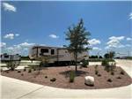 RV parked on lot near trees and gravel - thumbnail