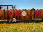 A dog cooling himself in the shade of a wood fence at SANDOLLAR RV PARK - thumbnail