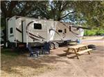 An RV, picnic table and chairs in a shaded site - thumbnail