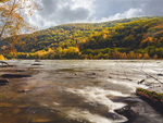 View of fall trees on a hill from the river at Country Roads Campground - thumbnail