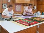 View larger image of Two ladies cutting fabric for a quilt at TIP O TEXAS RV RESORT image #5